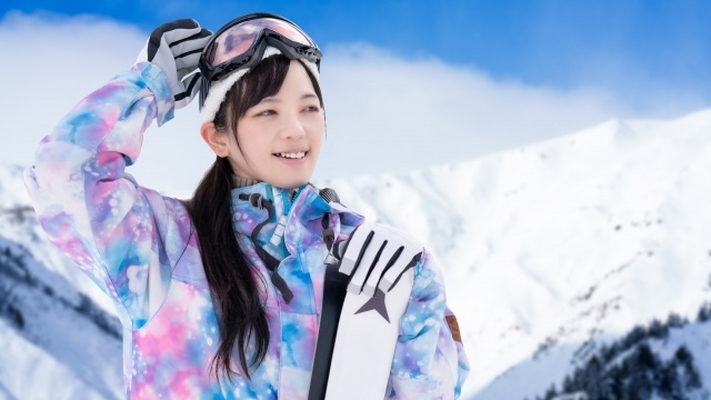 明るい色のスキーウェアを着てスノーボードを持つ女性